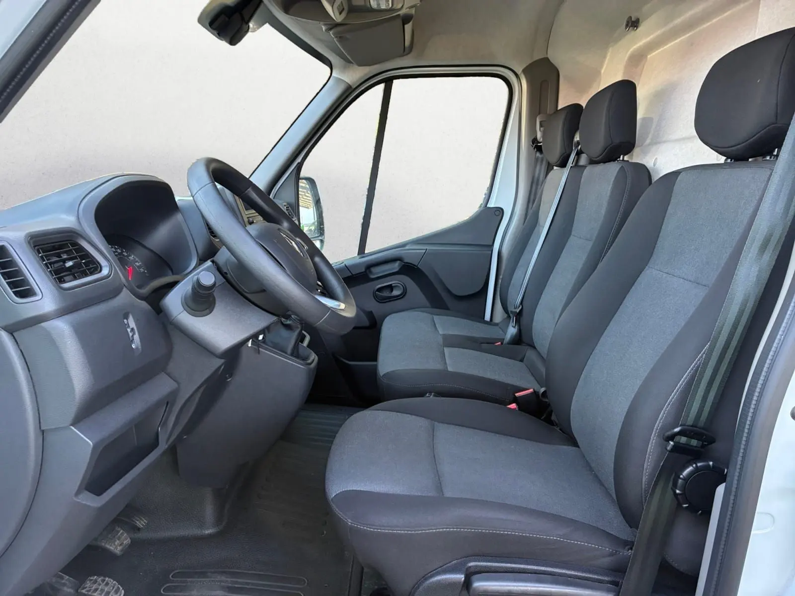 Vue intérieure côté conducteur du Renault Master blanc 2024, montrant les trois sièges en tissu gris et le tableau de bord.