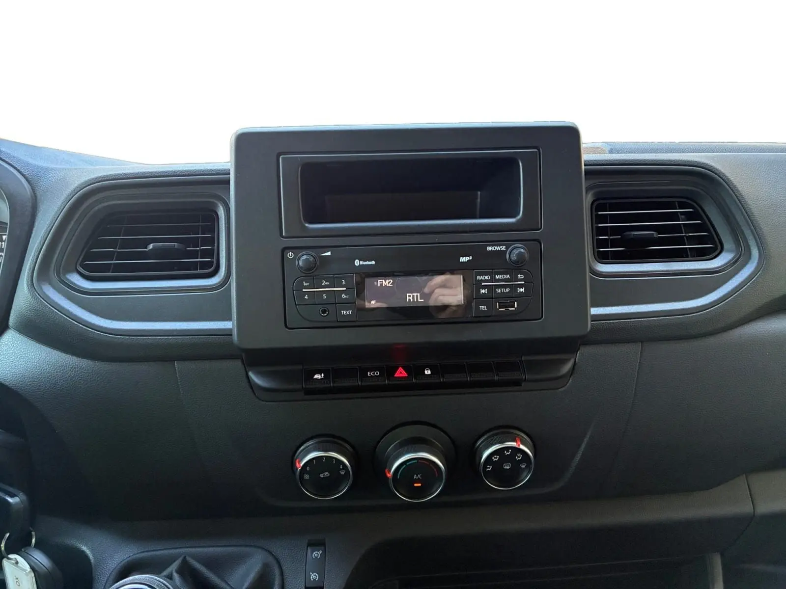 Vue rapprochée du tableau de bord noir du Renault Master 2024, avec radio, commandes climatisation et aérateurs.