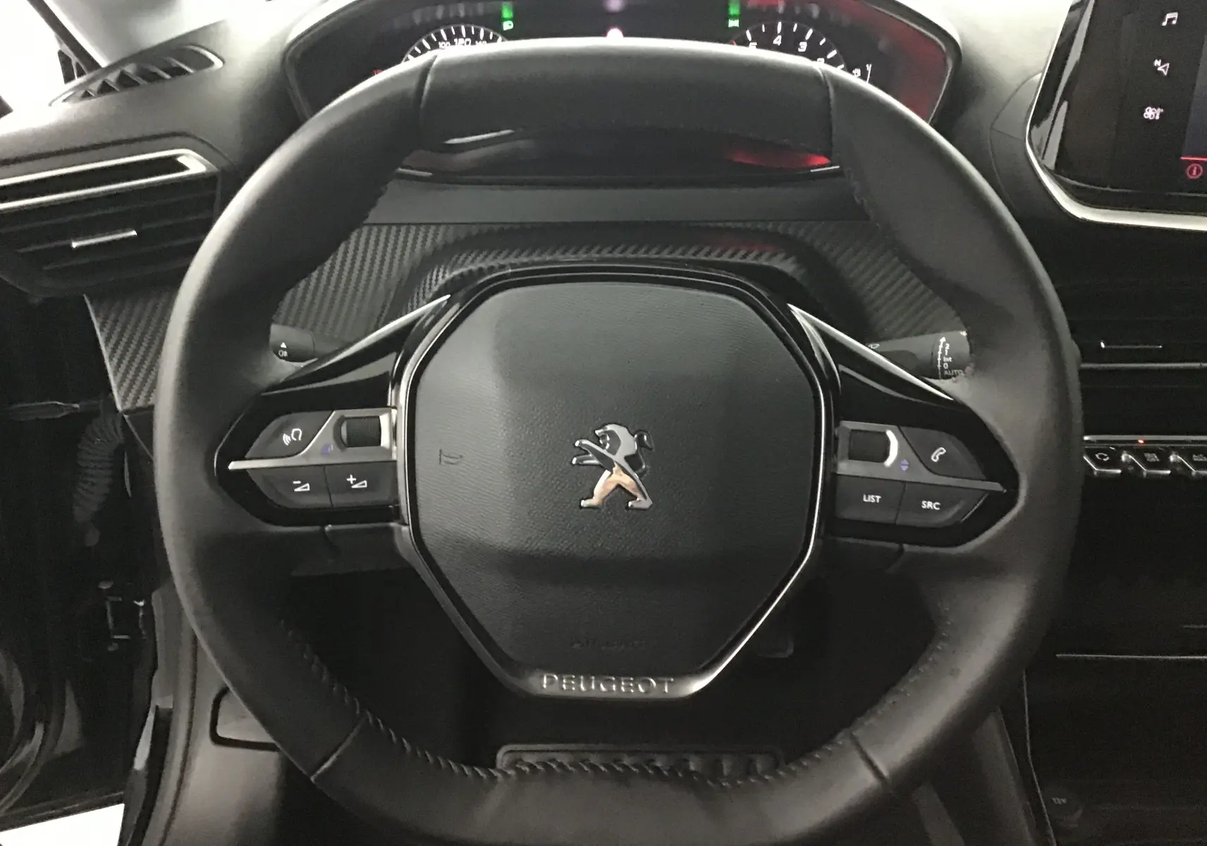 Vue rapprochée du volant cuir noir du Peugeot 208 2022 avec commandes intégrées et tableau de bord en arrière-plan.