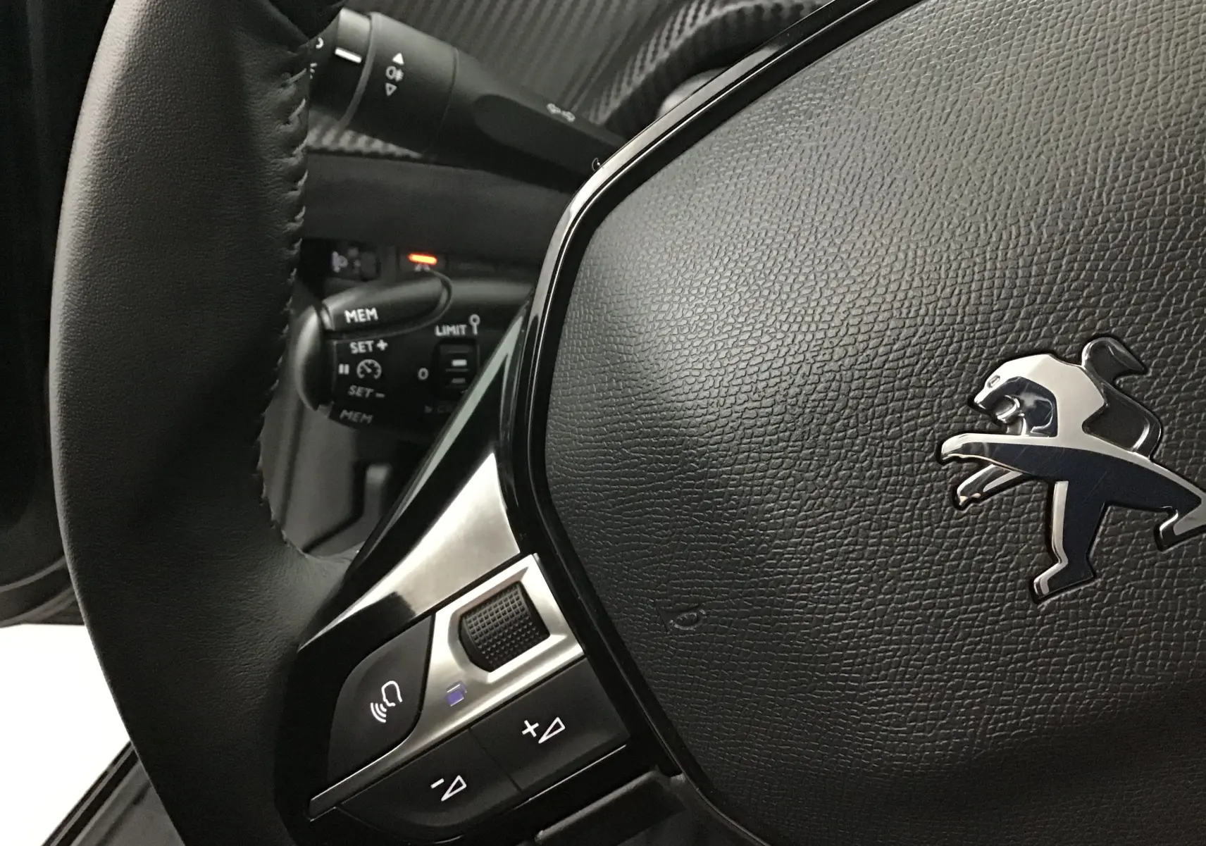 Gros plan sur le volant en cuir noir de la Peugeot 208 2022, avec commandes intégrées et logo lion argenté.