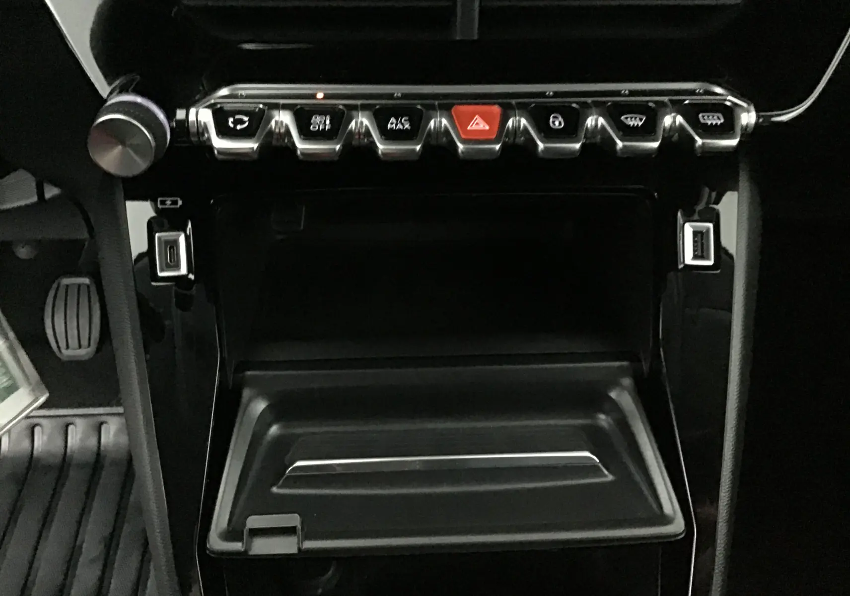 Vue rapprochée du tableau de bord noir de la Peugeot 208 2022, mettant en valeur les commandes chromées et le rangement ouvert.