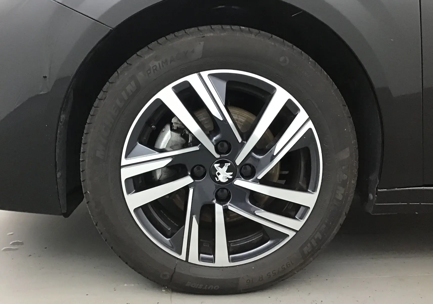 Gros plan sur la jante alliage bicolore avec logo Peugeot d'une 208 noire, côté arrière droit.