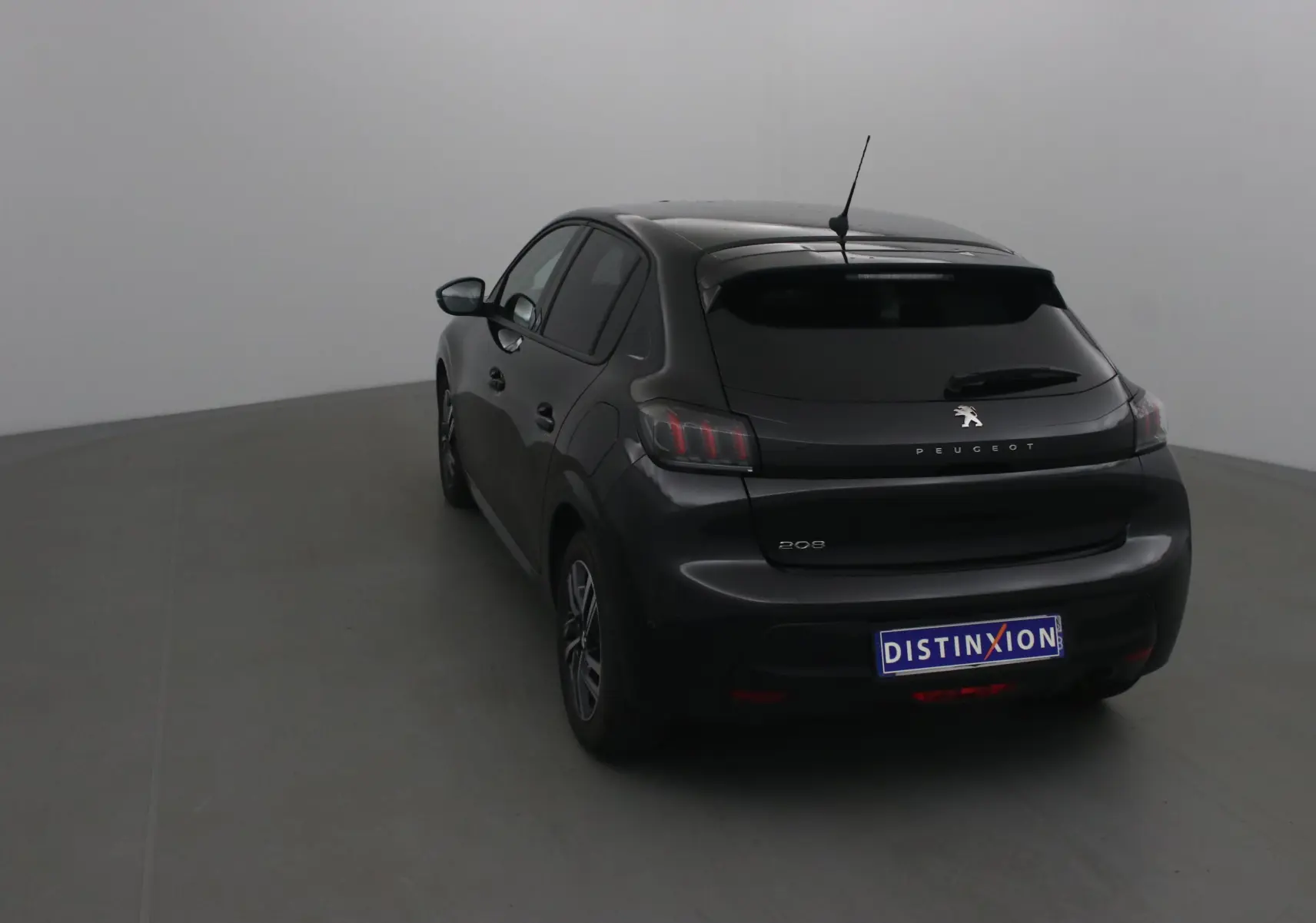 Vue 3/4 arrière gauche d'une Peugeot 208 noire 2022 avec feux arrière caractéristiques et antenne sur le toit.