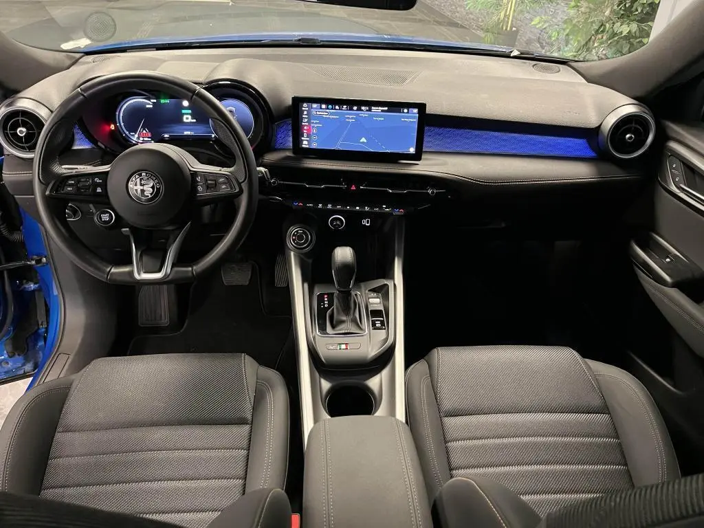 Vue intérieure avant de l'Alfa Romeo Tonale bleu, tableau de bord noir avec écran tactile et éclairage d'ambiance bleu.