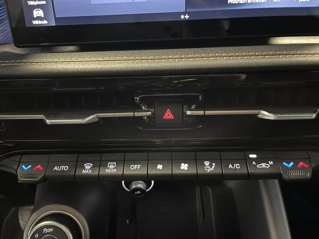 Gros plan sur la console centrale de l'Alfa Romeo Tonale bleu 2024, mettant en valeur les commandes de climatisation et le bouton de warning.
