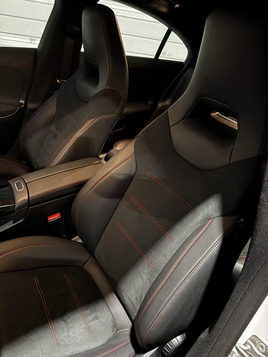 Vue intérieure rapprochée des sièges avant noirs avec surpiqûres rouges du Mercedes CLA 250 e AMG Line blanc 2023.
