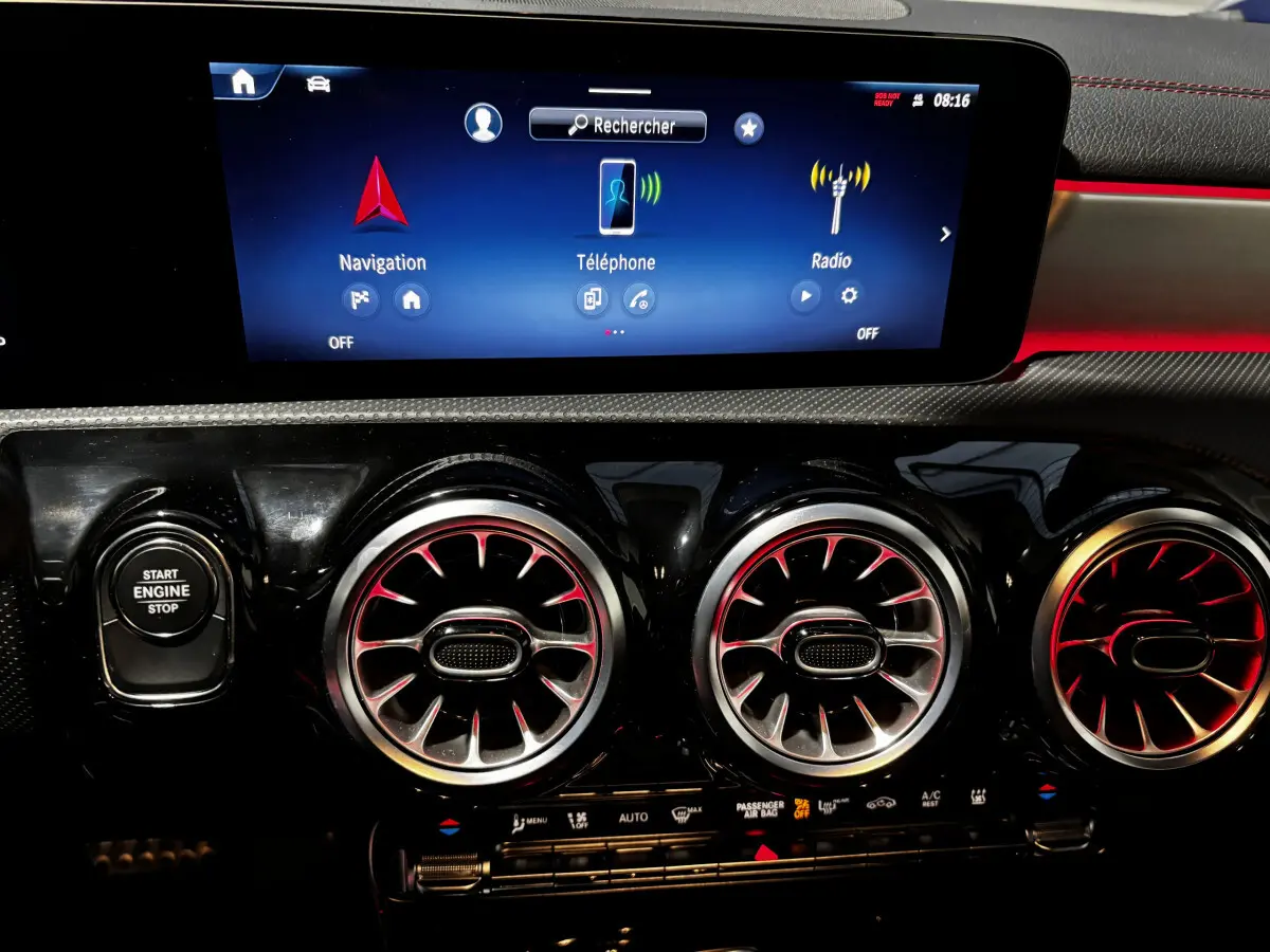 Vue rapprochée du tableau de bord noir avec écran tactile et aérateurs ronds à éclairage rouge d'une Mercedes CLA 250 e AMG Line blanche.