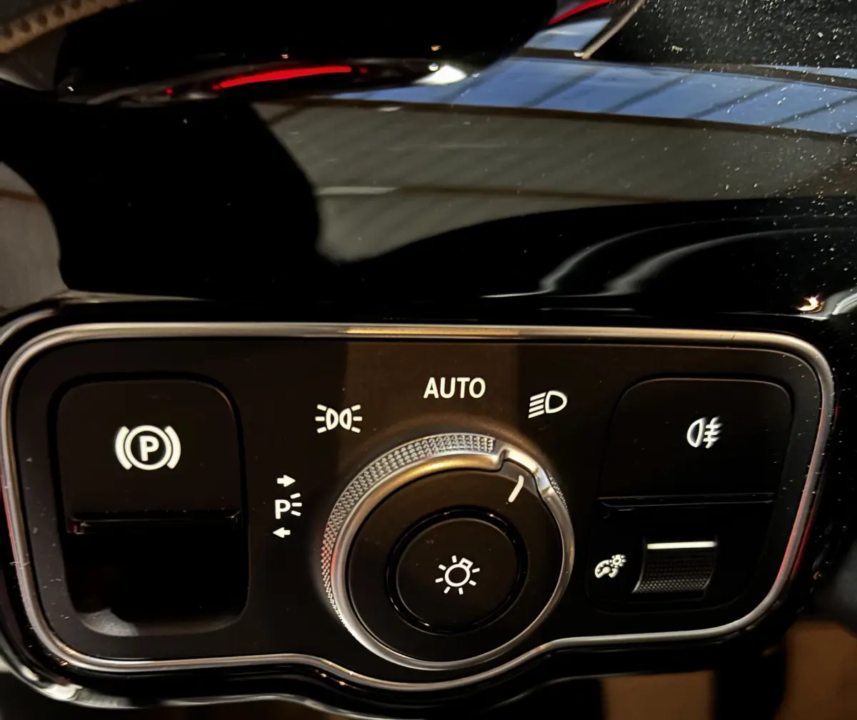 Gros plan sur la commande des phares et du frein à main électrique dans l’habitacle noir d’une Mercedes CLA 250 e AMG Line blanche.