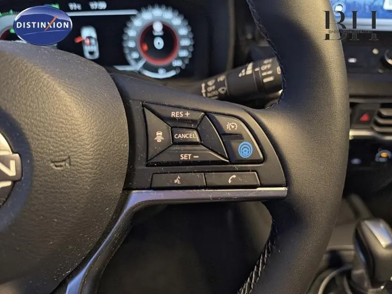 Gros plan sur les commandes au volant d’un Nissan Juke 1.6 Hybrid Tekna 2025, intérieur noir avec tableau de bord numérique.