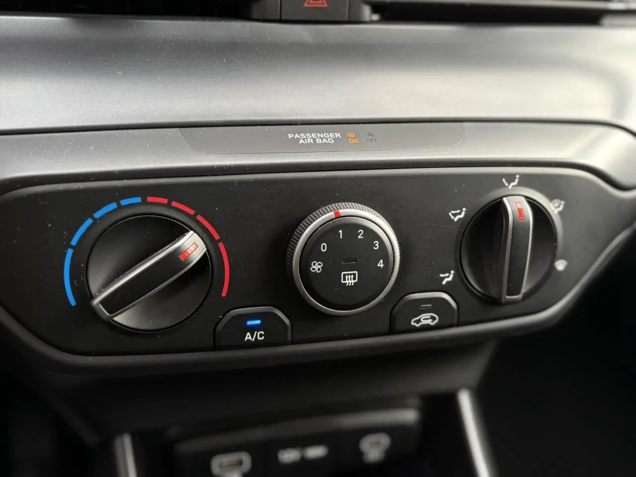 Gros plan sur les commandes de climatisation manuelle noires de la Hyundai i20 Rouge Dragon Metal, avec réglages température et ventilation.
