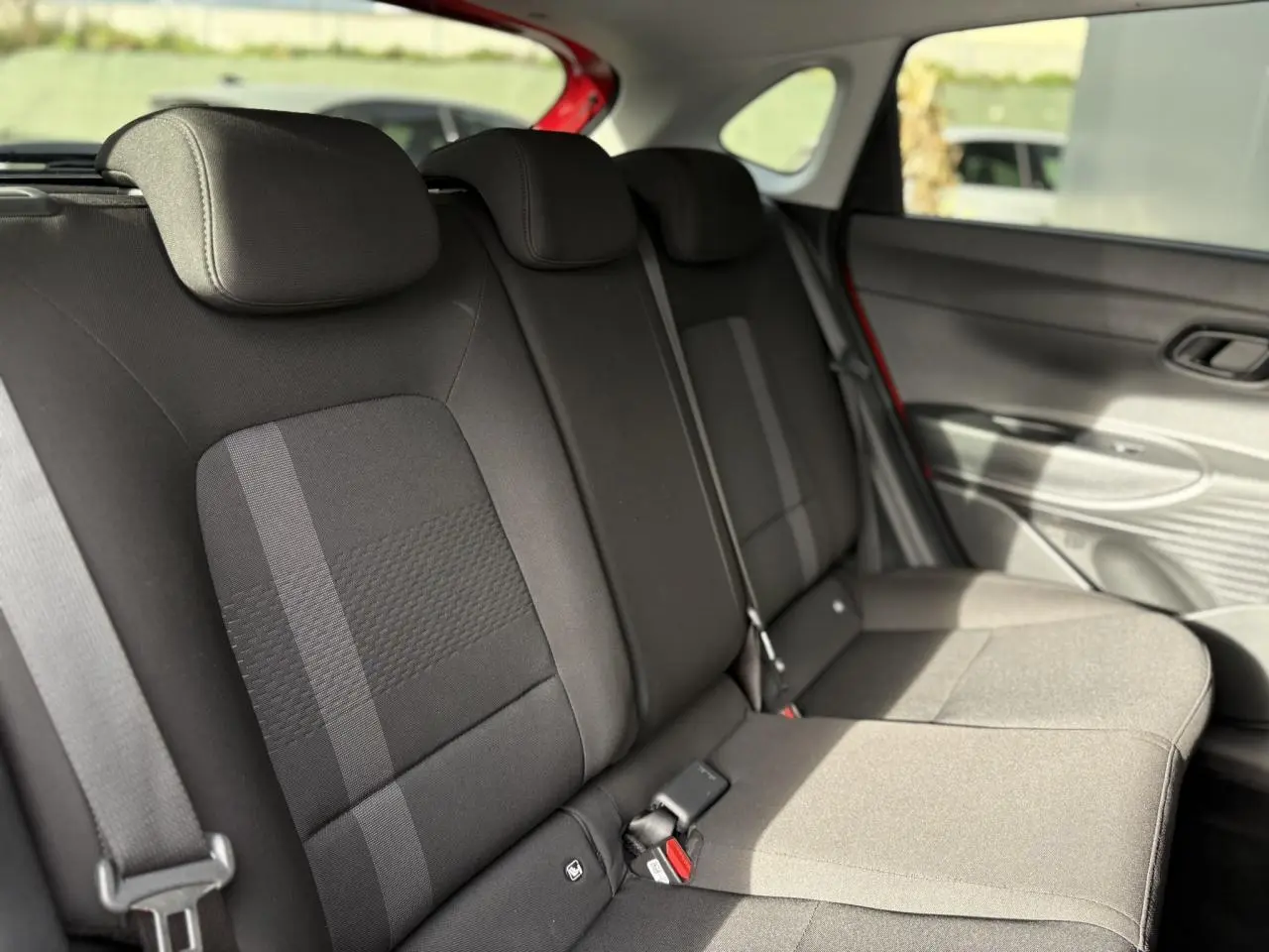 Vue intérieure des sièges arrière noirs de la Hyundai i20 2025, avec ceinture et porte arrière rouge Dragon Metal visible.
