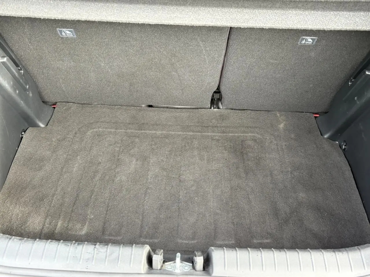 Coffre ouvert vu de l'arrière d'une Hyundai i20 Rouge Dragon Metal, montrant le tapis de coffre et banquette arrière.