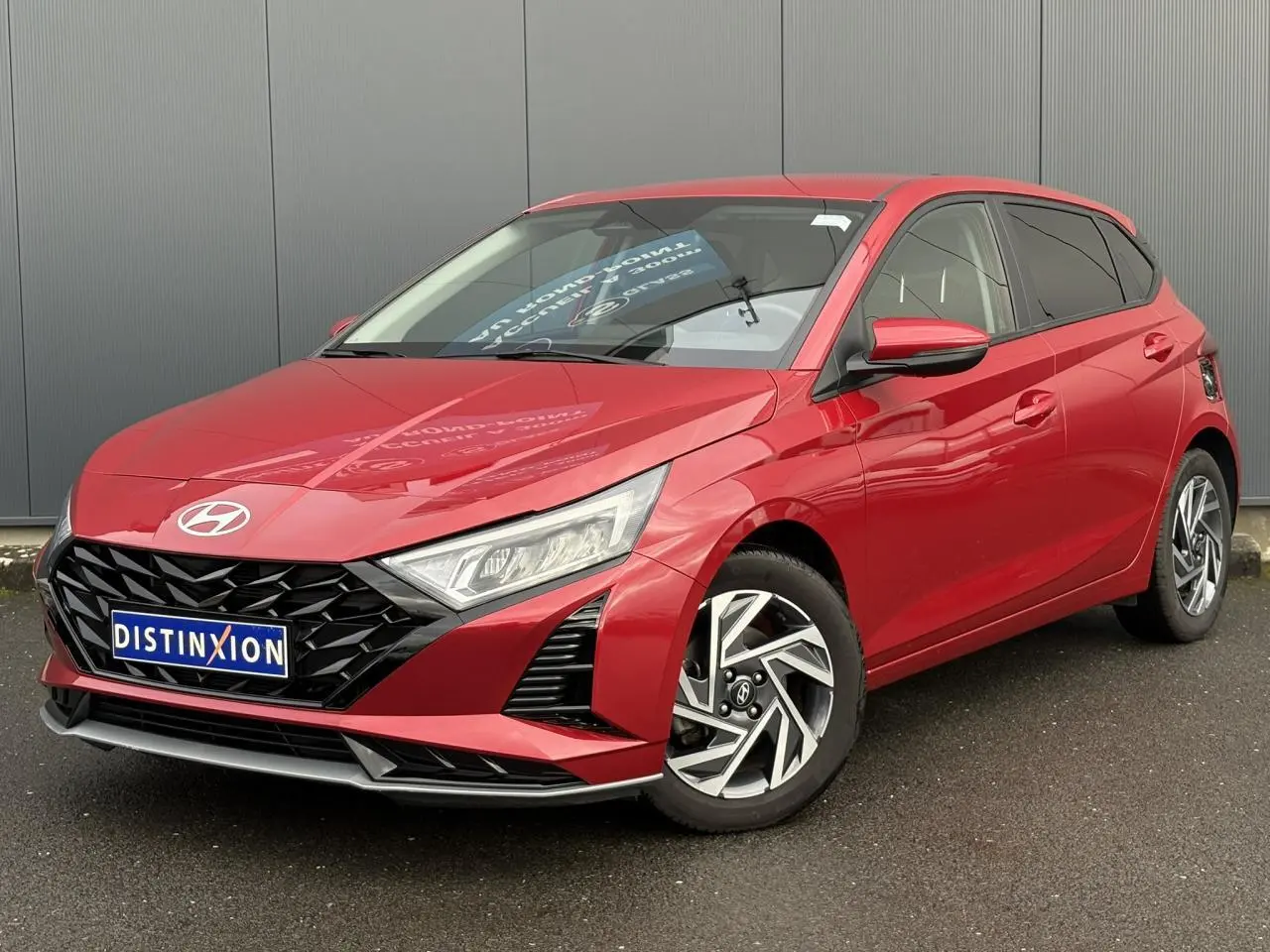 Vue 3/4 avant droite d'une Hyundai i20 2025 rouge Dragon Metal avec jantes alliage diamantées et calandre noire.