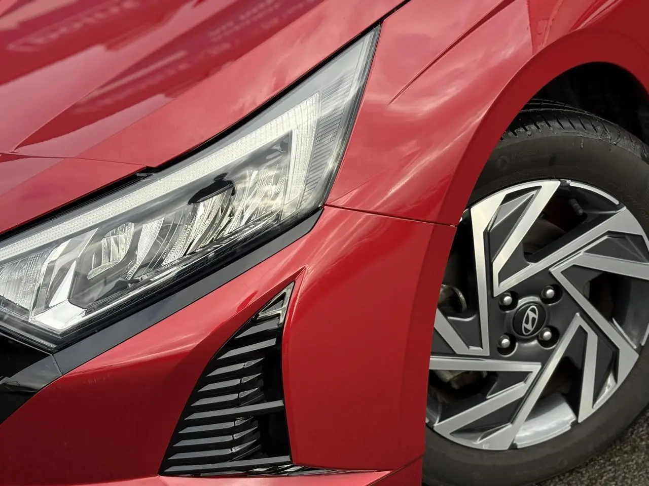 Gros plan sur l'avant droit rouge Dragon Metal d'une Hyundai i20 2025, mettant en valeur le phare LED et la jante alliage diamantée.