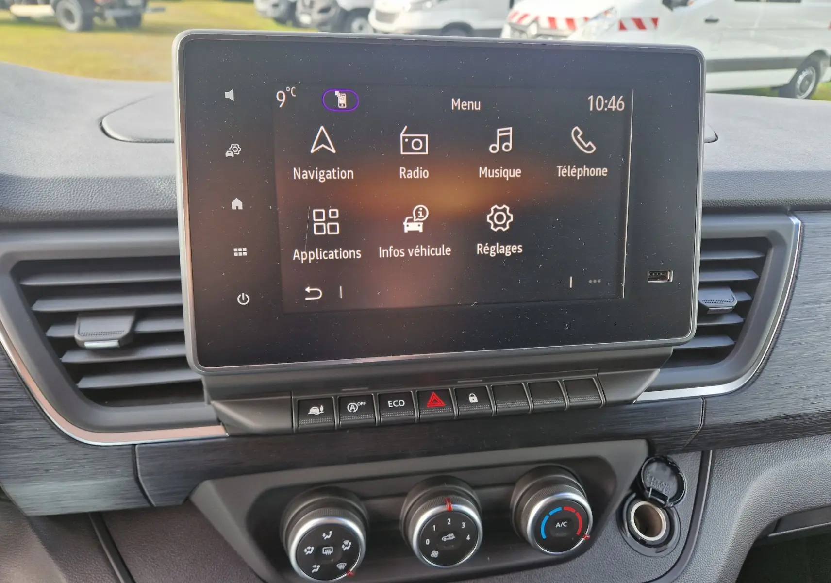Écran tactile central du Nissan Primastar 2025 avec commandes climatisation et finition bois, vue intérieure avant.