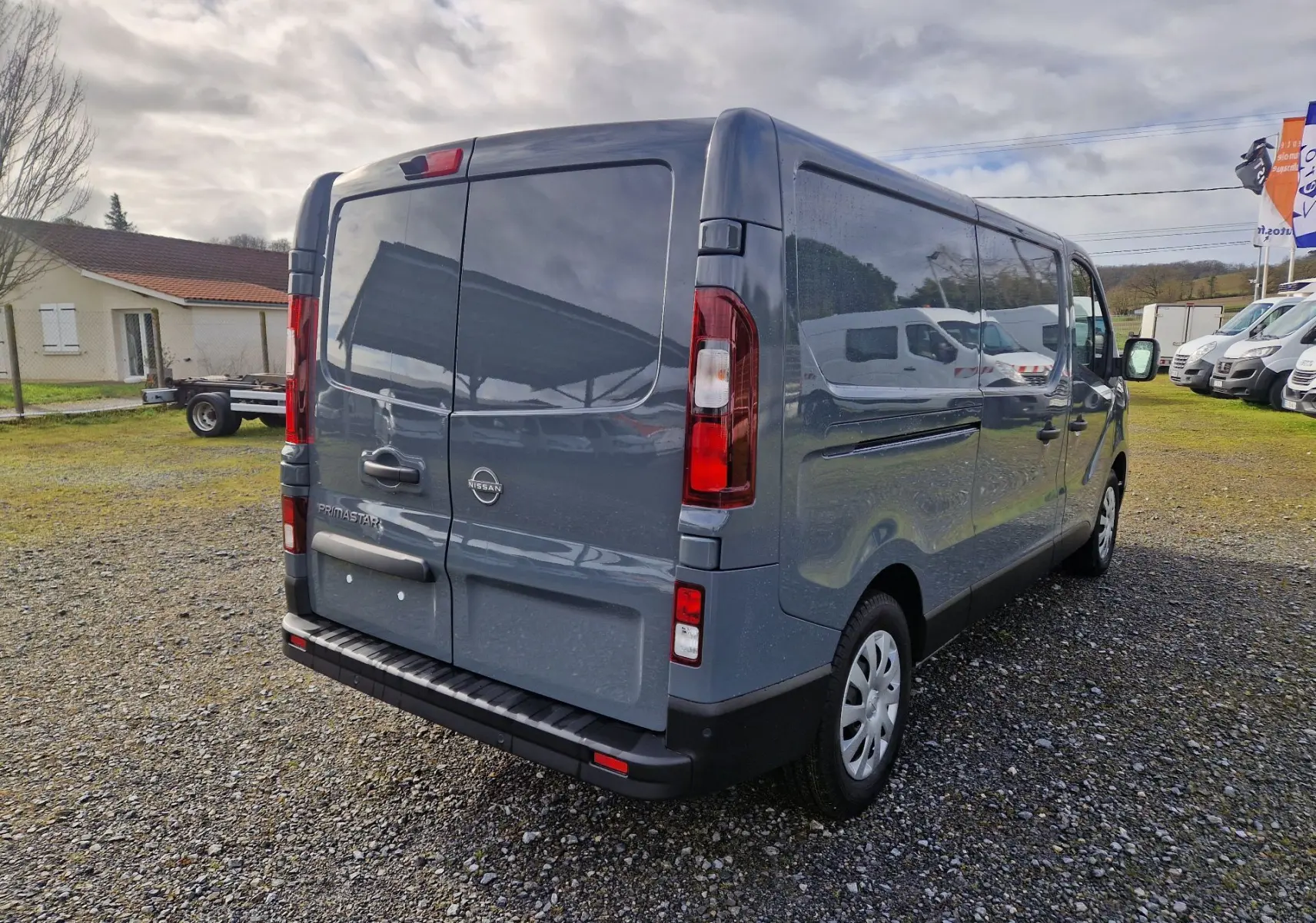 Vue 3/4 arrière droite d’un utilitaire Nissan Primastar gris urbain avec portes arrière battantes et vitres teintées.