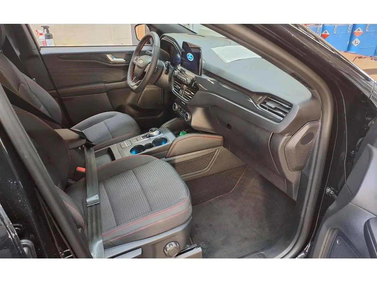 Vue intérieure côté conducteur du Ford Kuga noir Agathe 2024, mettant en valeur les sièges tissu avec surpiqûres rouges et la console centrale moderne.