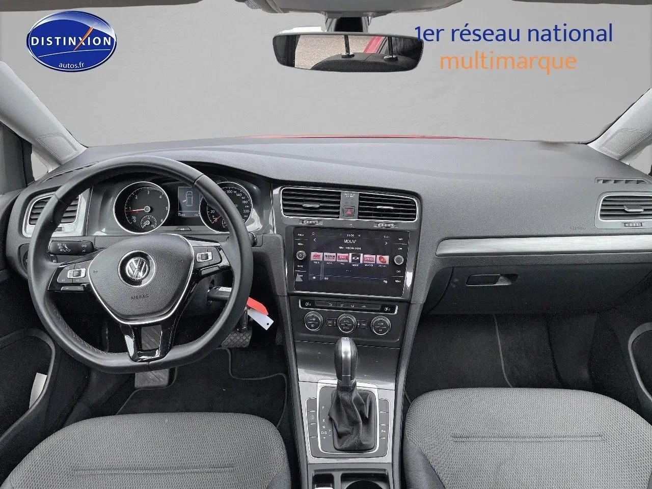 Vue intérieure frontale du tableau de bord et volant noir d'une Volkswagen Golf VII rouge, avec écran tactile central et boîte automatique.