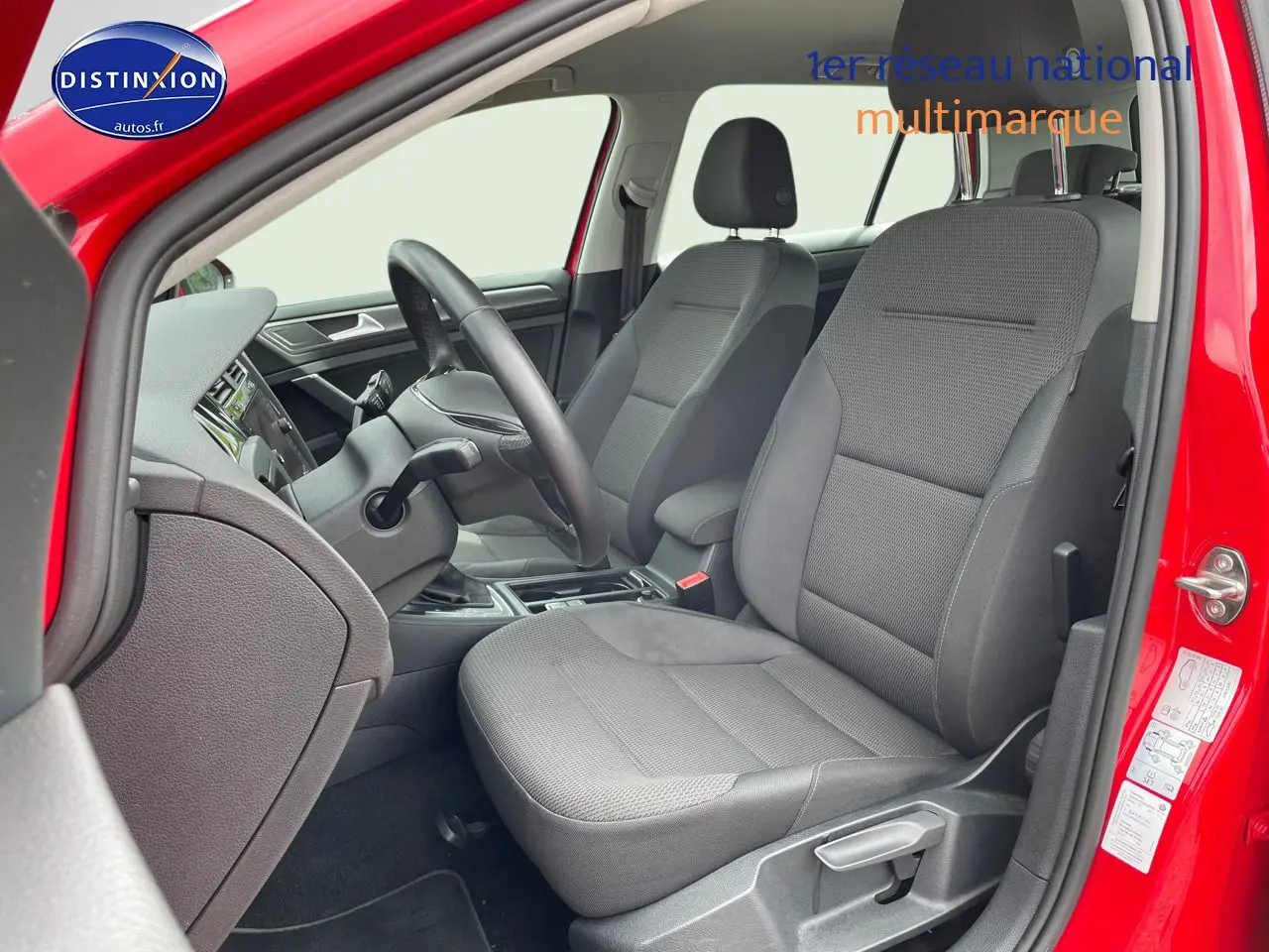 Vue intérieure côté conducteur d’une Volkswagen Golf rouge de 2018, sièges tissu gris et tableau de bord noir.