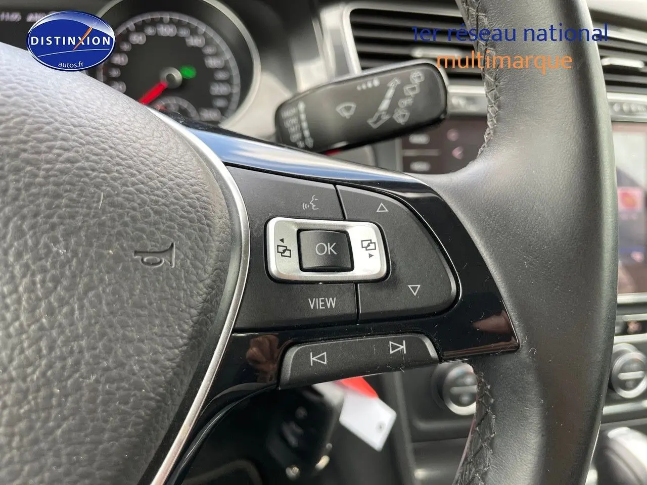 Gros plan sur les commandes au volant côté gauche d’une Volkswagen Golf rouge, intérieur cuir noir visible en arrière-plan.