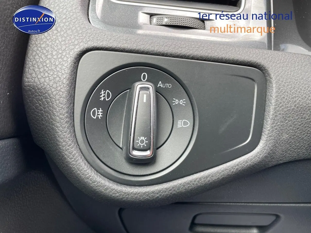 Gros plan sur le bouton de commande des phares dans l’habitacle noir d’une Volkswagen Golf VII rouge.
