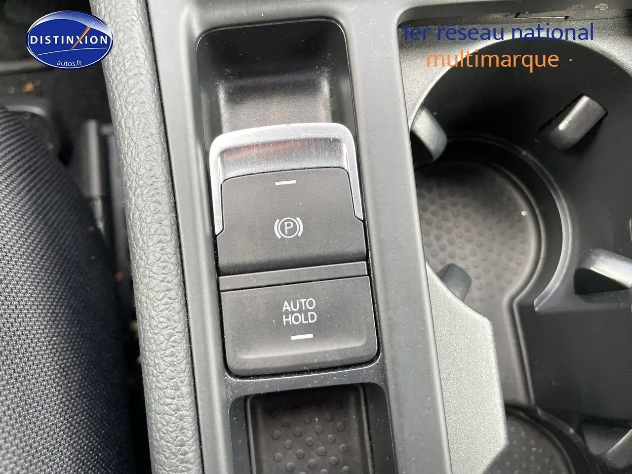 Gros plan sur la console centrale de la Volkswagen Golf rouge, montrant les boutons frein à main électronique et auto hold.