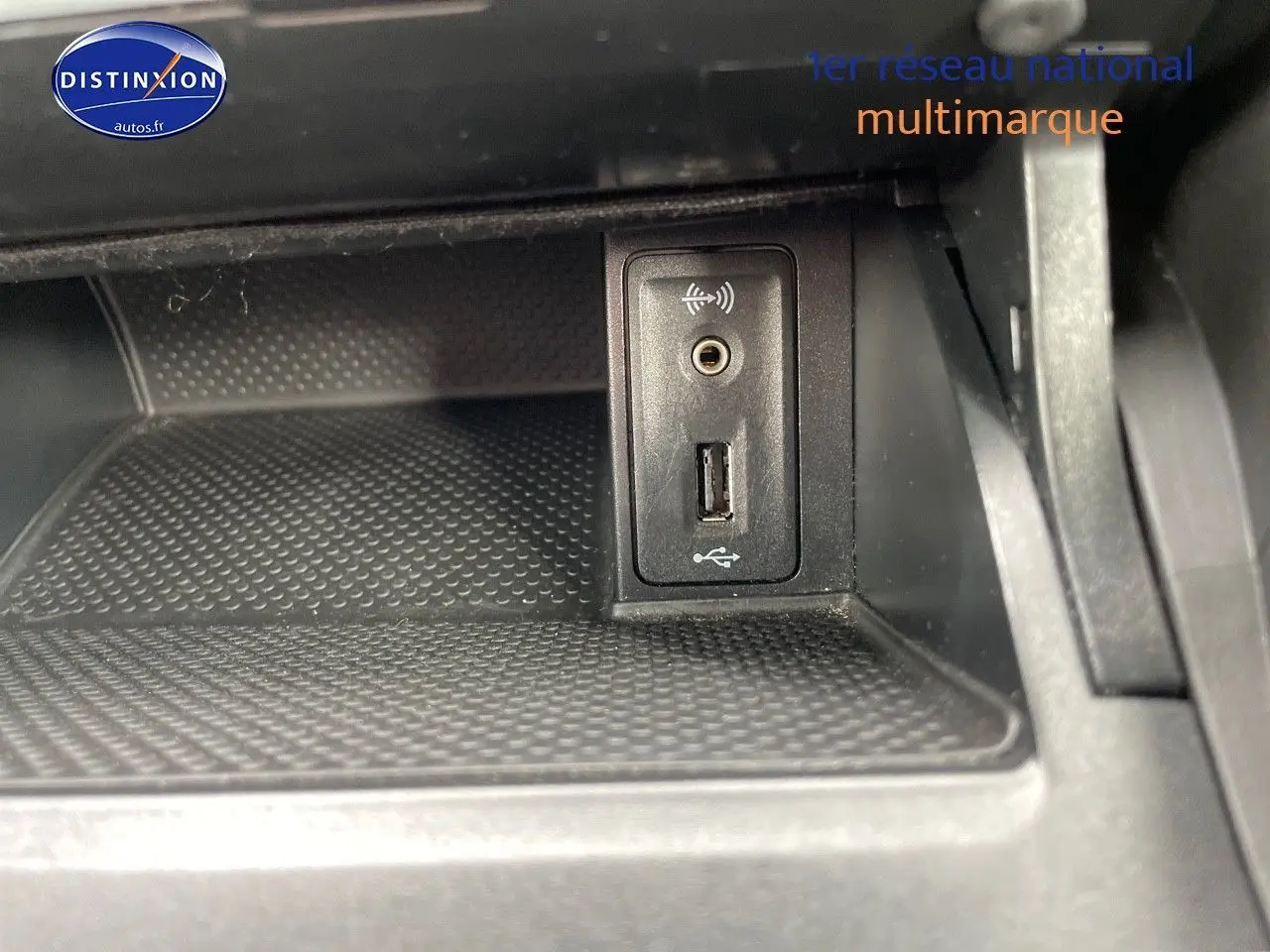 Vue rapprochée de la prise USB et jack audio dans le compartiment intérieur noir d'une Volkswagen Golf VII rouge.