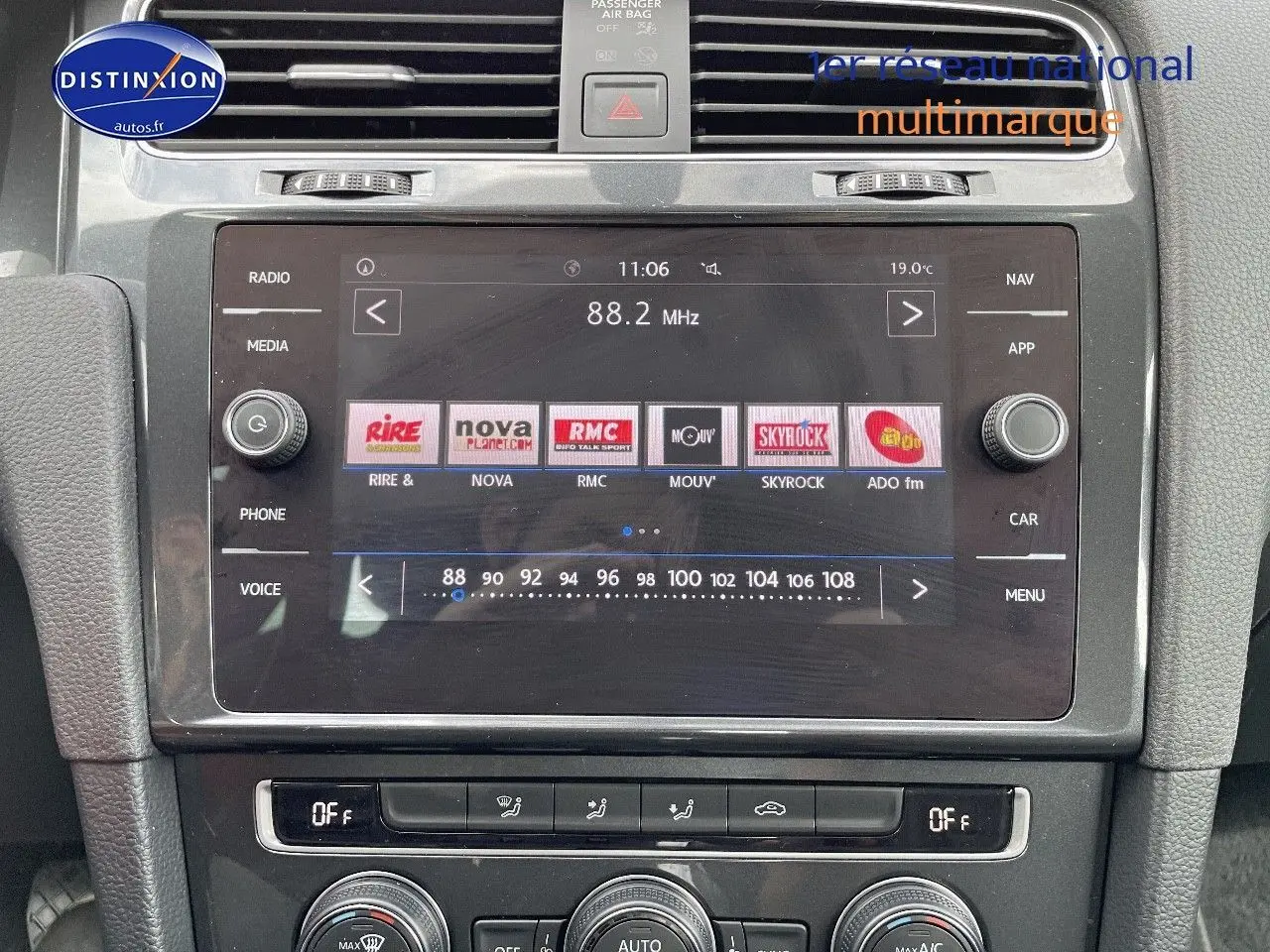 Vue rapprochée de la console centrale de la Volkswagen Golf VII rouge, mettant en valeur l’écran tactile multimédia et les commandes de climatisation.