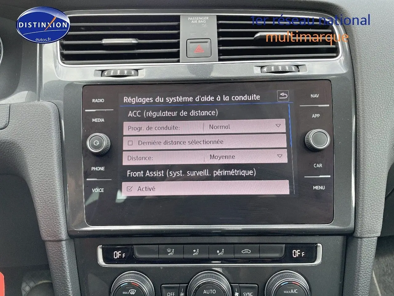 Vue rapprochée de l’écran tactile central et de la console de la Volkswagen Golf VII rouge, affichant les réglages d’aide à la conduite.