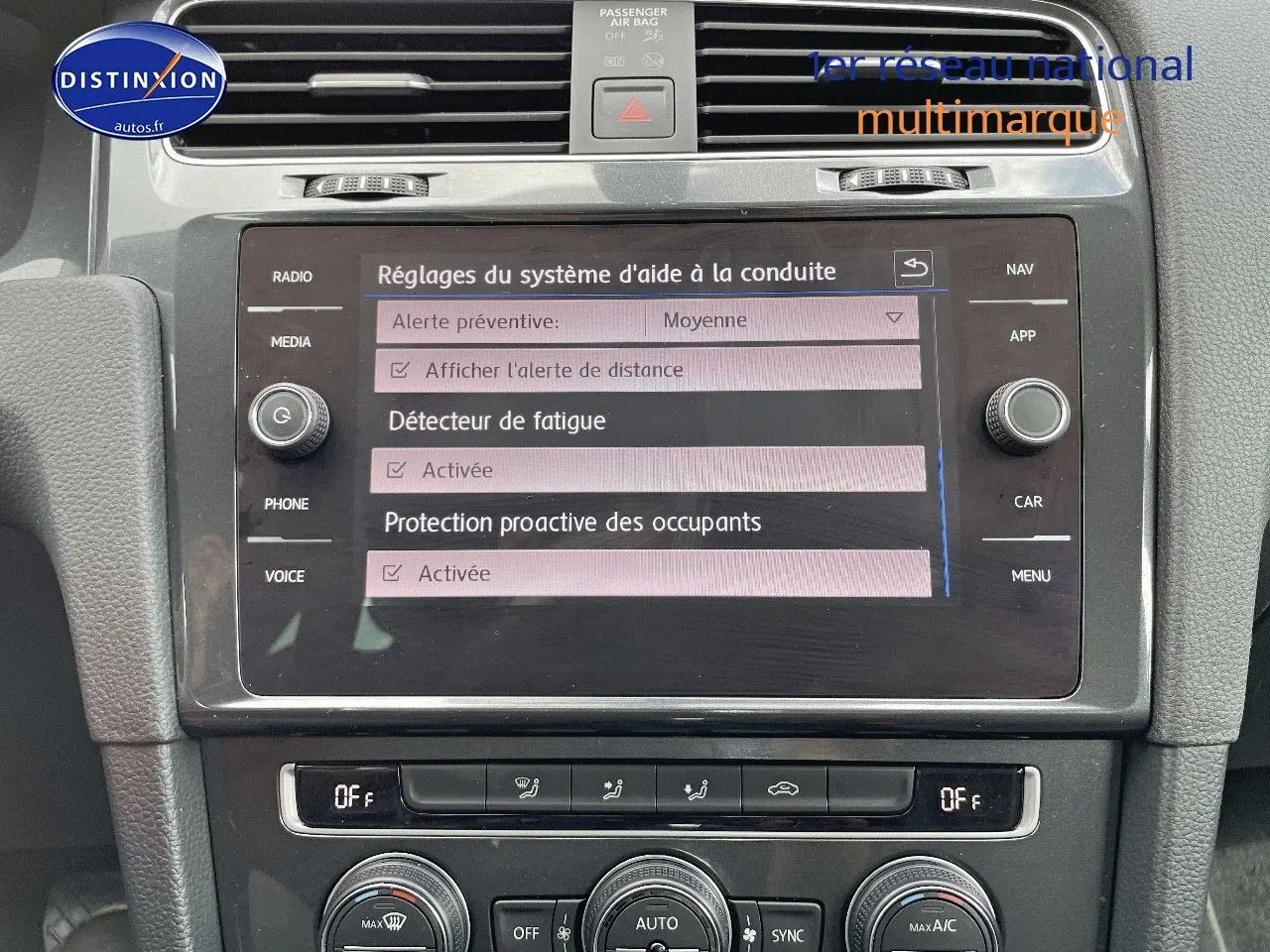 Vue rapprochée de l’écran central tactile et de la console de la Volkswagen Golf rouge, affichant les réglages d’aide à la conduite.