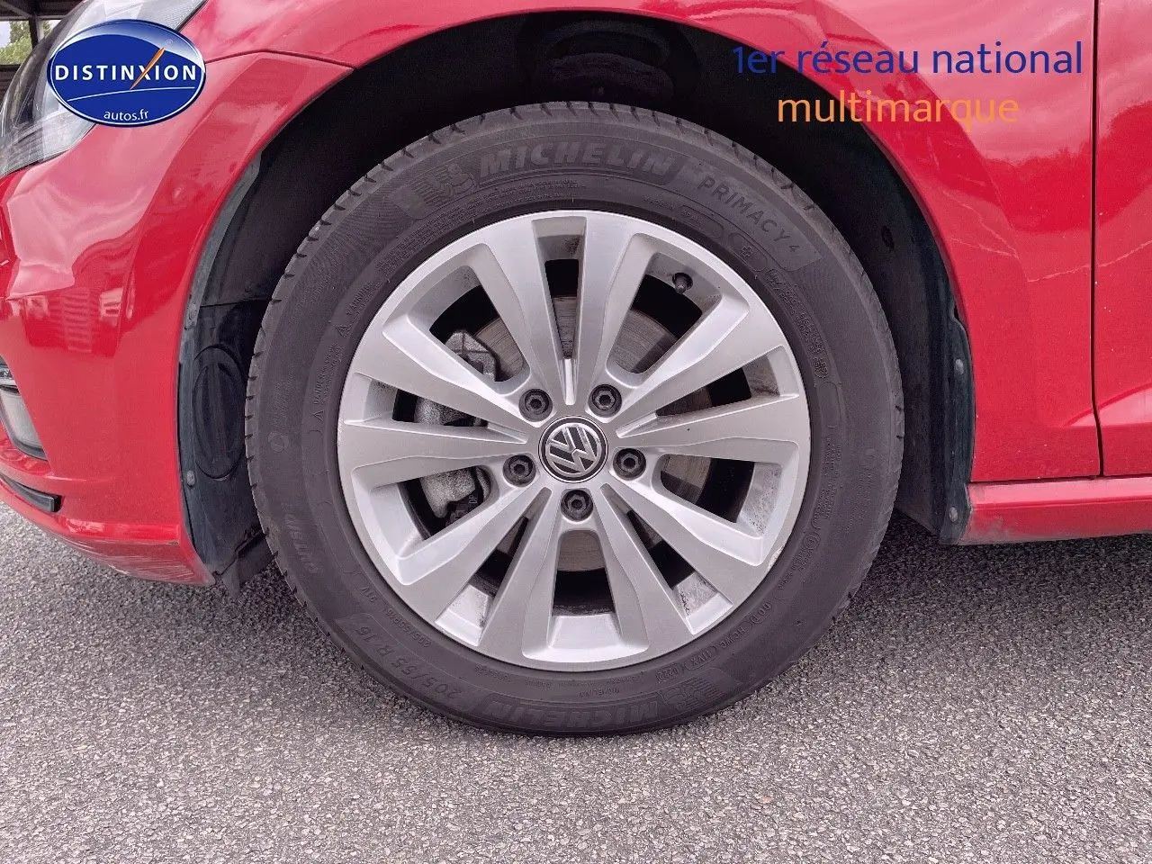 Gros plan sur la roue avant gauche d'une Volkswagen Golf rouge, mettant en valeur la jante alliage et le pneu Michelin.