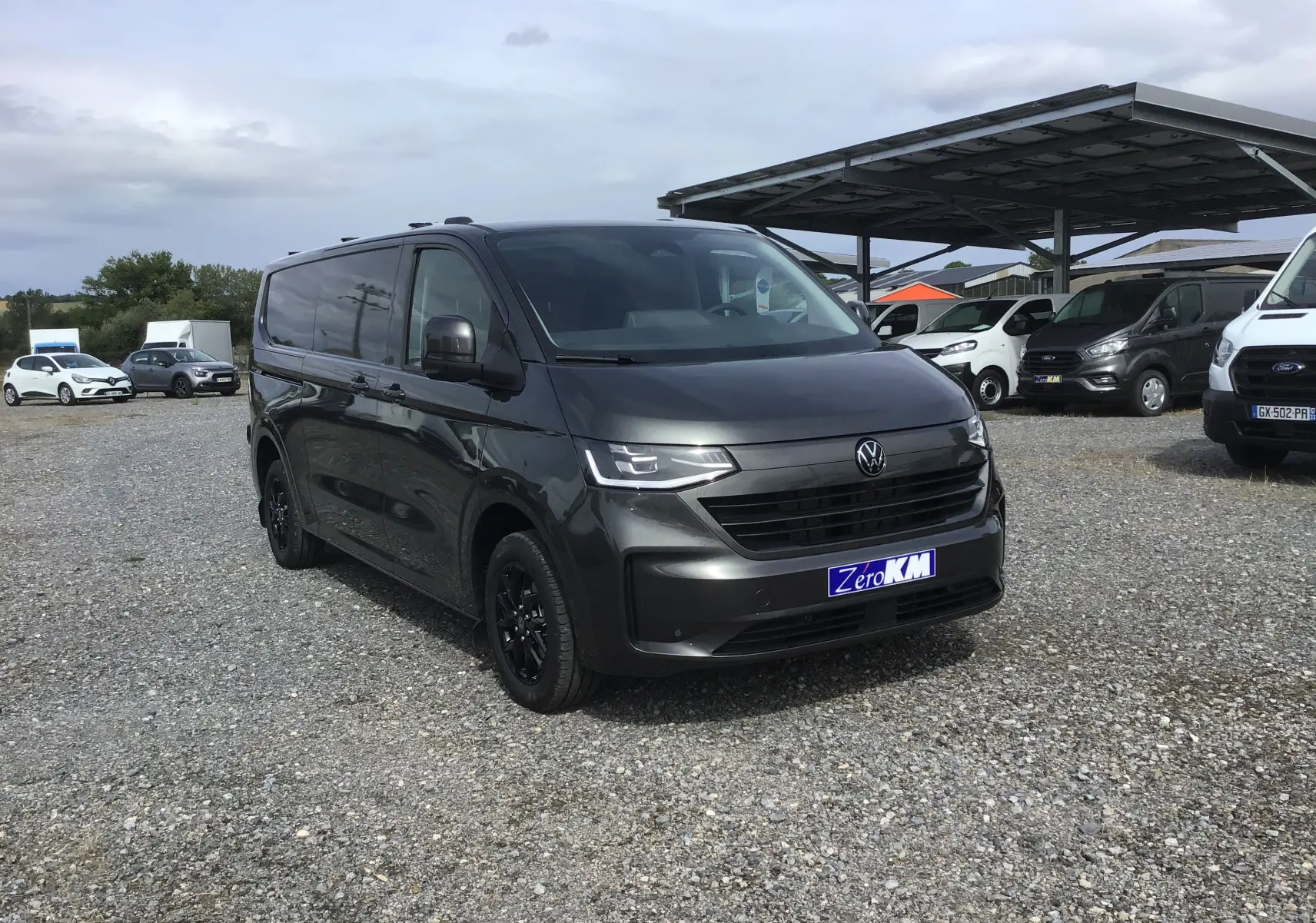 Volkswagen Transporter T7 gris anthracite vu en 3/4 avant droit avec jantes noires et calandre moderne.