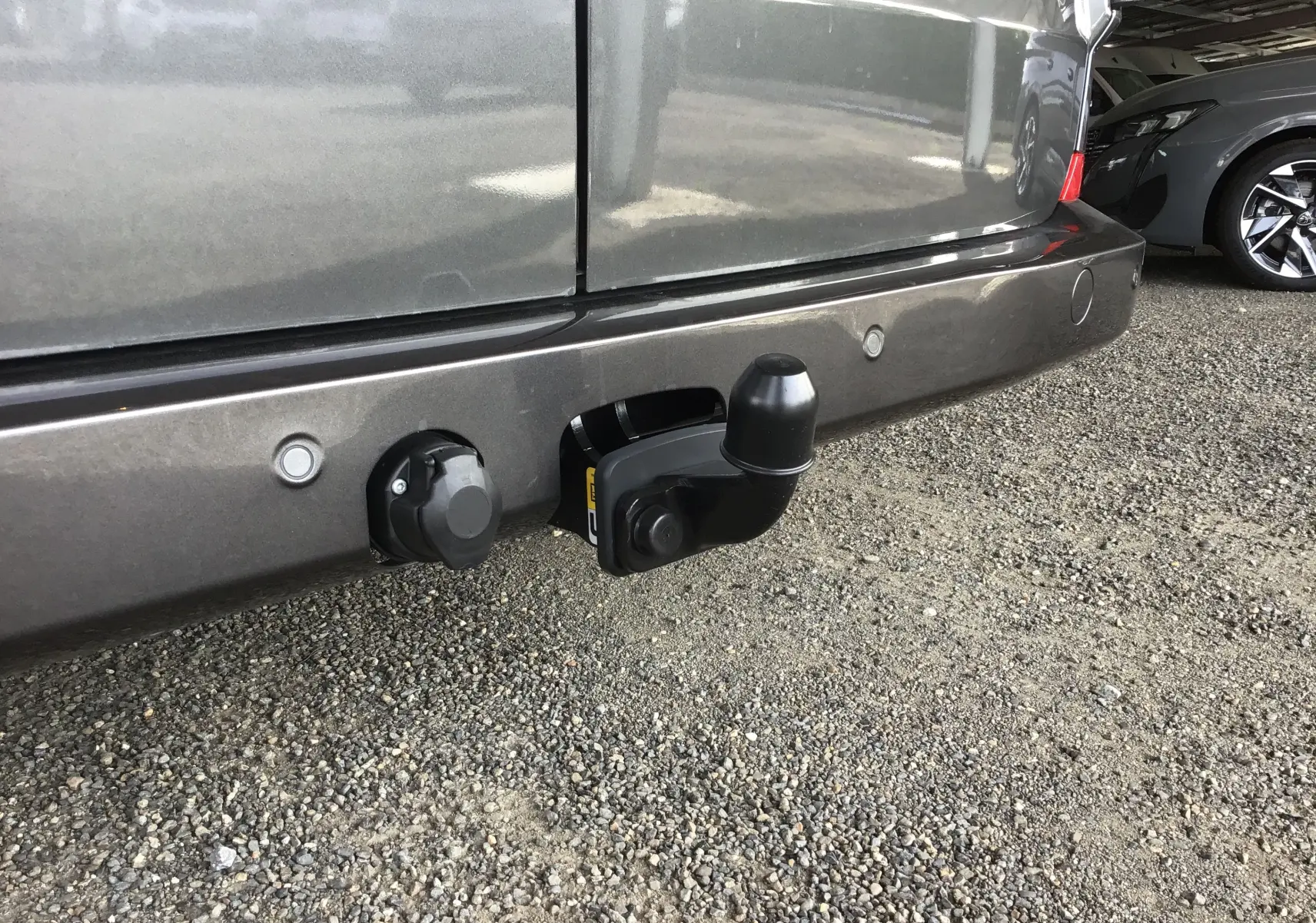 Gros plan sur l'attelage arrière gris anthracite du Volkswagen Transporter T7 avec prises électriques intégrées.