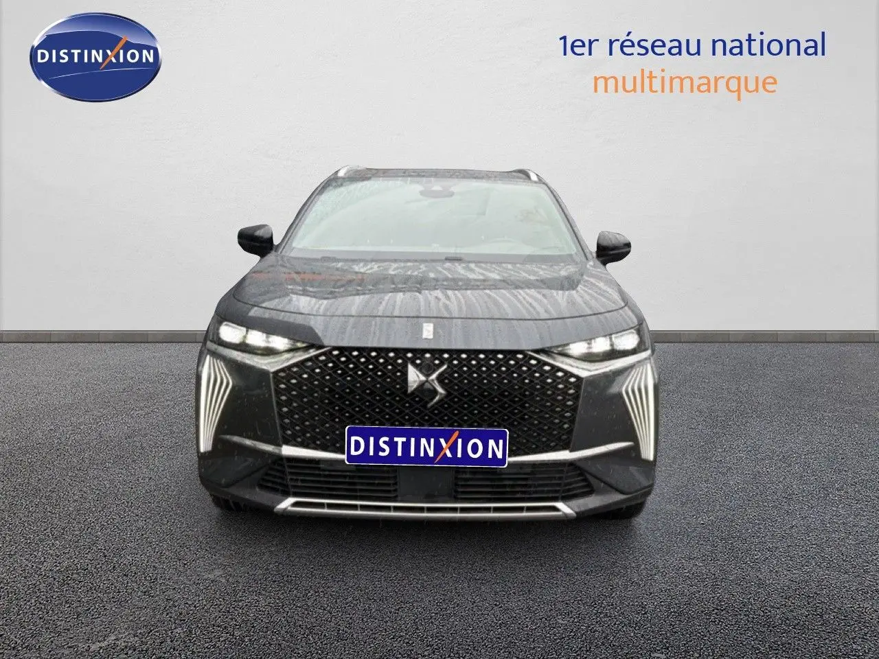 Vue de face du DS7 gris titane métal avec sa calandre distinctive et ses feux LED verticaux allumés.