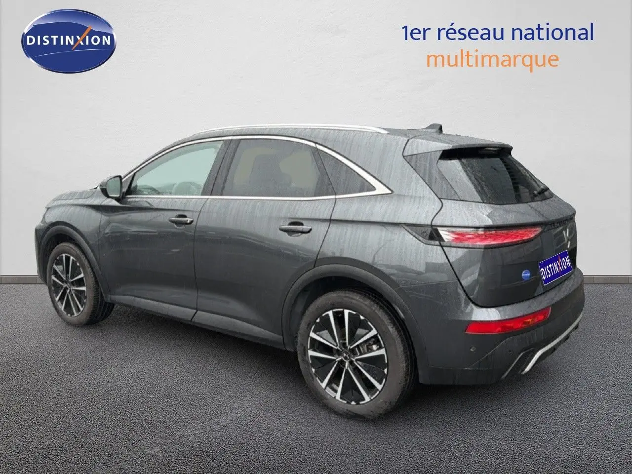 Vue 3/4 arrière droite d'un DS7 2024 gris titane métal avec jantes bi-ton et feux arrière LED allumés.