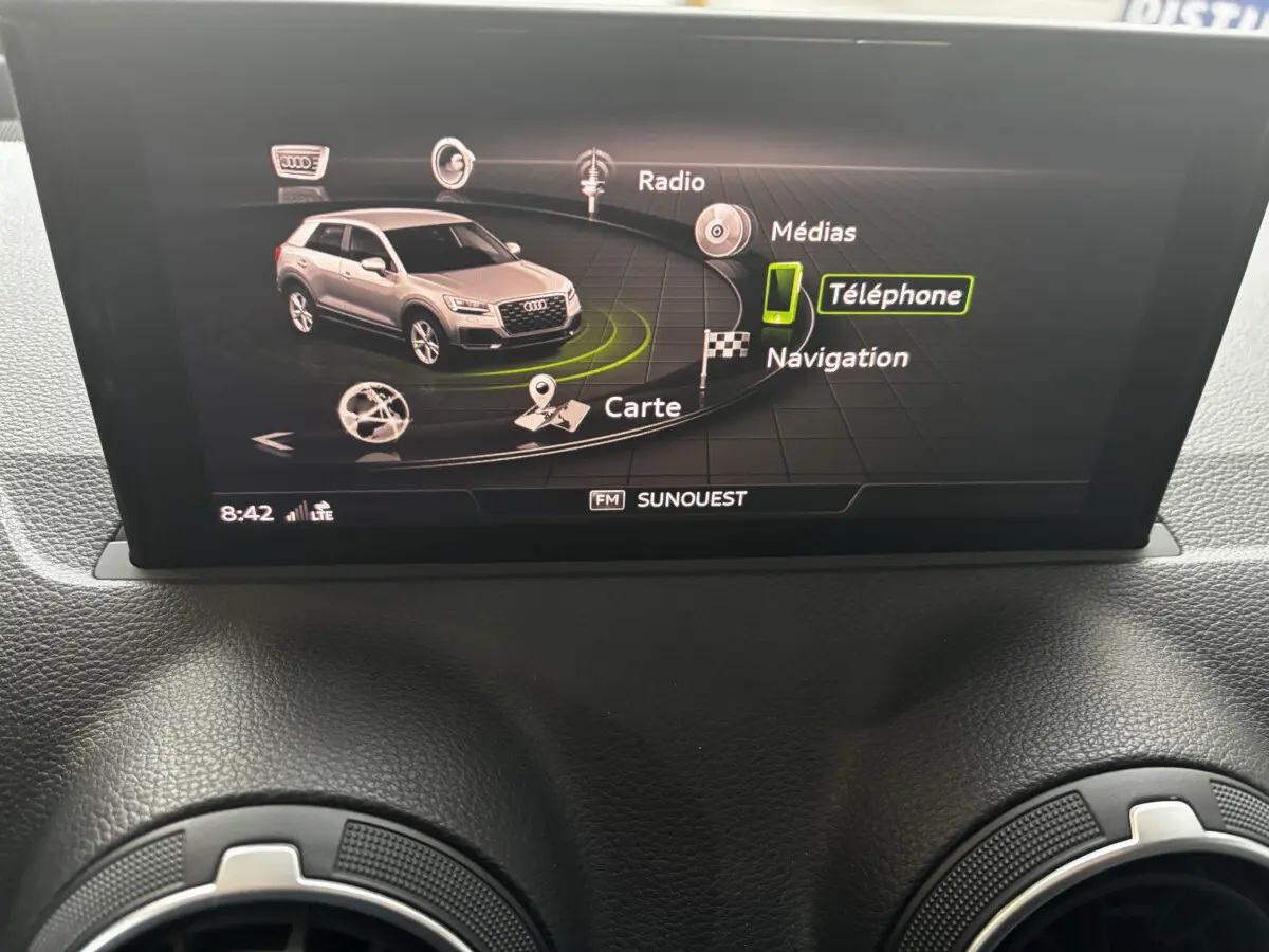 Écran central affichant le menu multimédia avec une Audi Q2 grise vue de 3/4 avant sur l'interface.