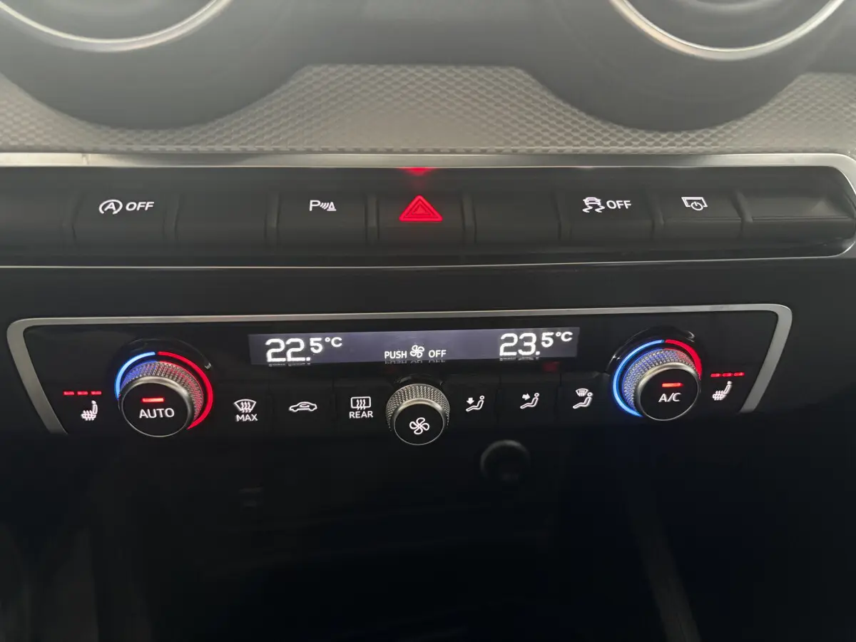 Gros plan sur la console centrale de l’Audi Q2 noire, montrant la climatisation digitale bi-zone avec commandes rotatives et boutons lumineux.