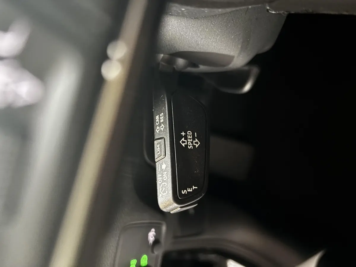 Gros plan sur la commande de régulateur de vitesse au volant d’un Audi Q2 noir, version 35 TFSI S Line.