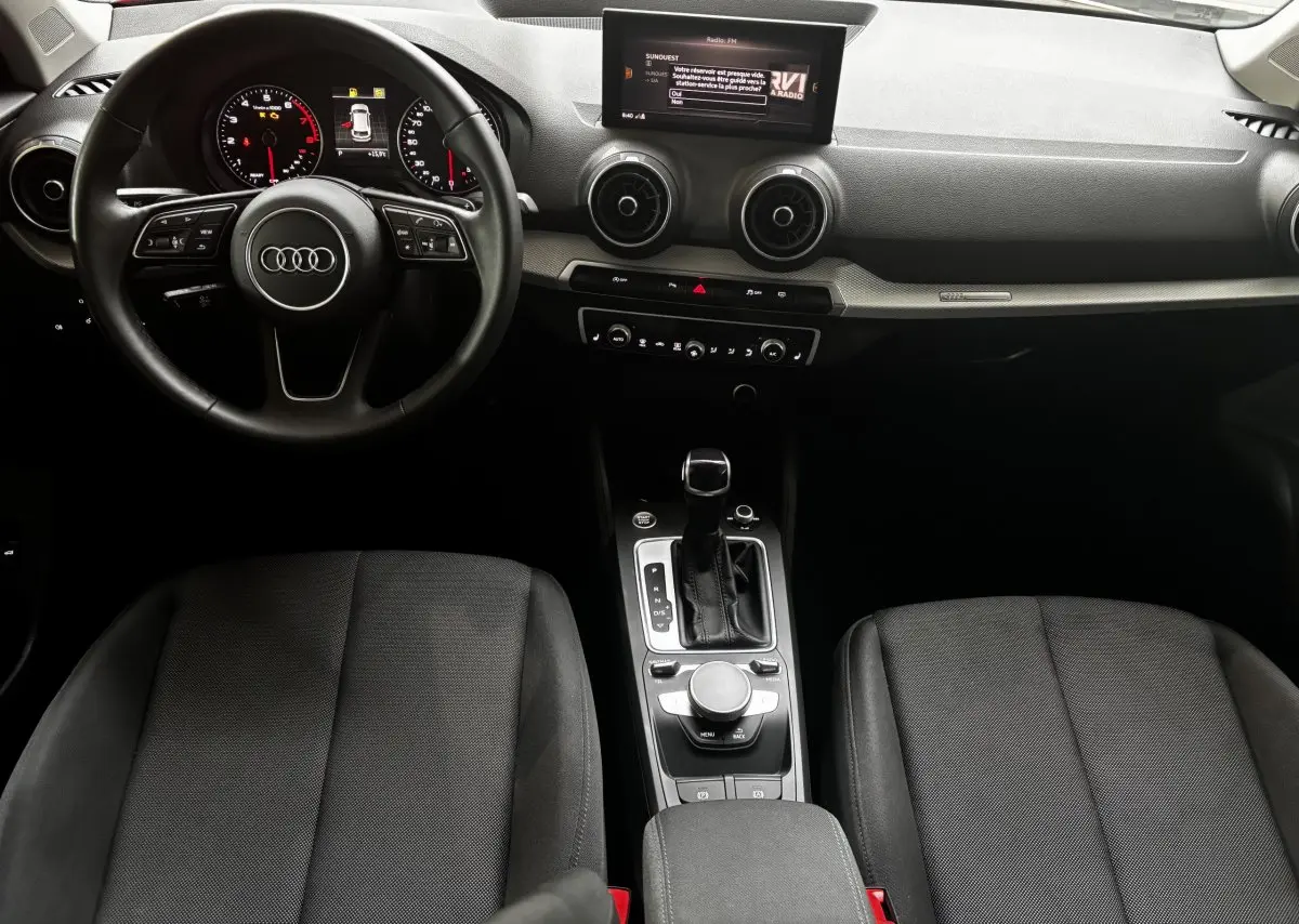 Vue intérieure de l'Audi Q2 35 TFSI S Line 2023, tableau de bord noir avec volant cuir et console centrale moderne.