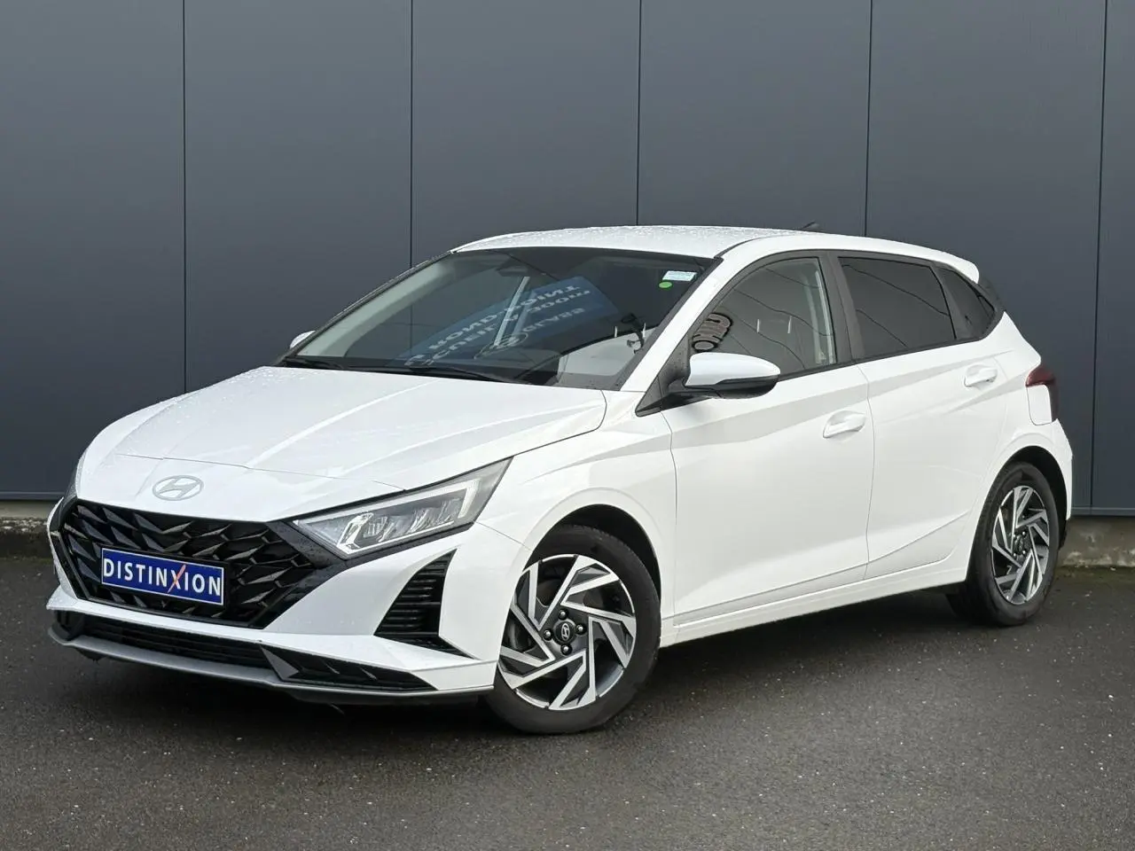 Vue 3/4 avant gauche d'une Hyundai i20 blanche Atlas avec jantes alliage diamantées et calandre noire distinctive.