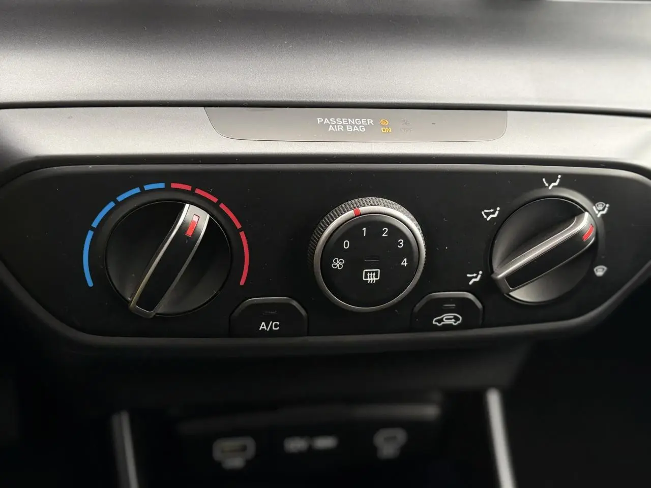 Vue rapprochée du tableau de bord noir de la Hyundai i20 2025 montrant les commandes manuelles de climatisation.