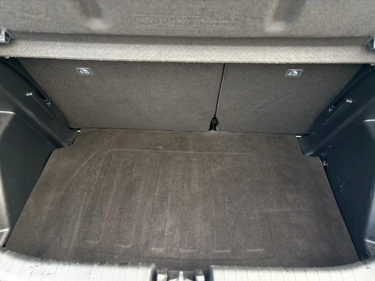 Coffre vide vu de dessus d'une Hyundai i20 2025, tapis de sol noir et habillage intérieur sombre.