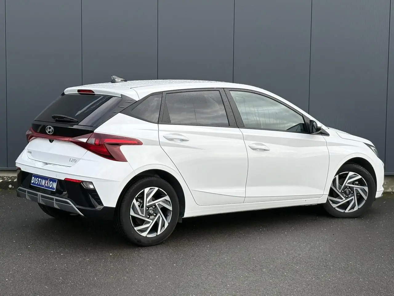 Vue 3/4 arrière droite d'une Hyundai i20 blanche Atlas avec jantes alliage 16'' diamantées et vitres surteintées.