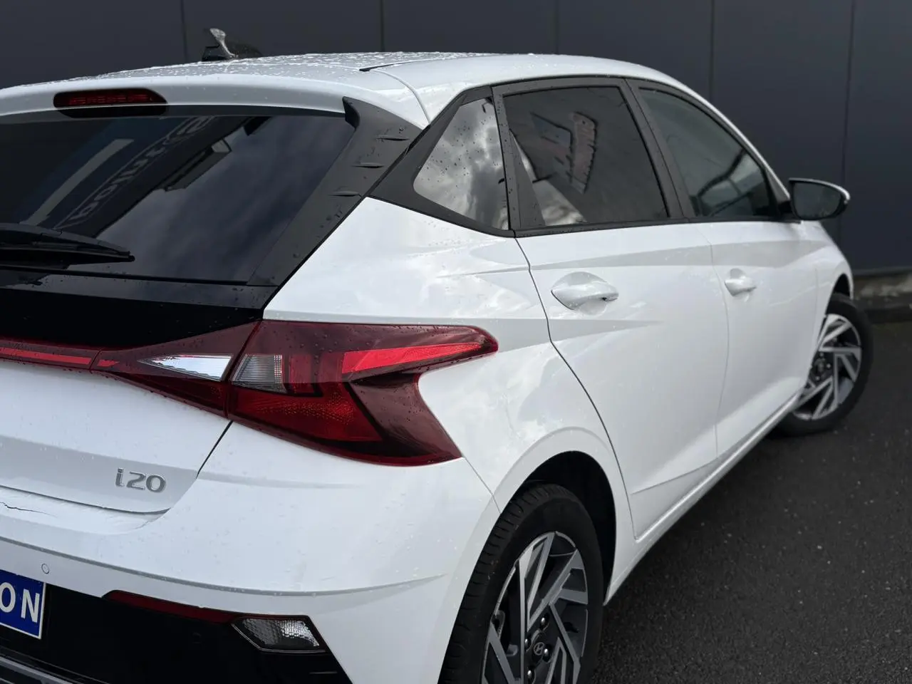 Vue 3/4 arrière droite d'une Hyundai i20 blanche Atlas avec jantes alliage 16'' diamantées et vitres surteintées.