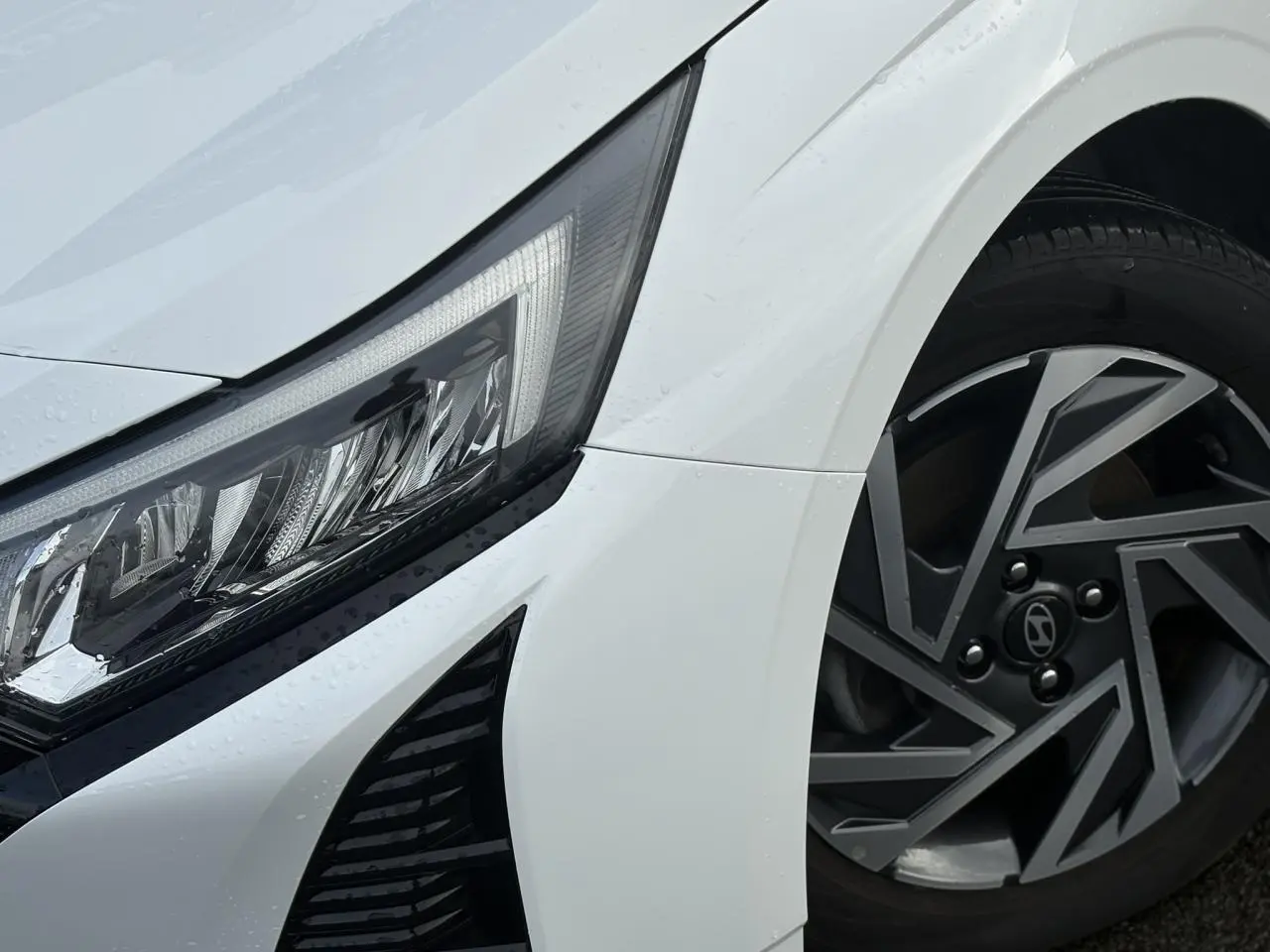 Gros plan sur l'avant droit blanc Atlas de la Hyundai i20 2025, mettant en valeur le phare LED et la jante alliage diamantée.