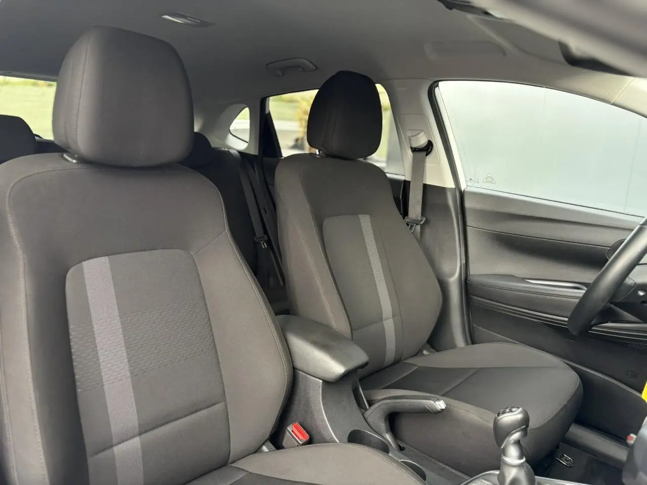 Vue intérieure côté droit des sièges avant noirs avec accoudoir central et levier de vitesses manuel d'une Hyundai i20 2025.