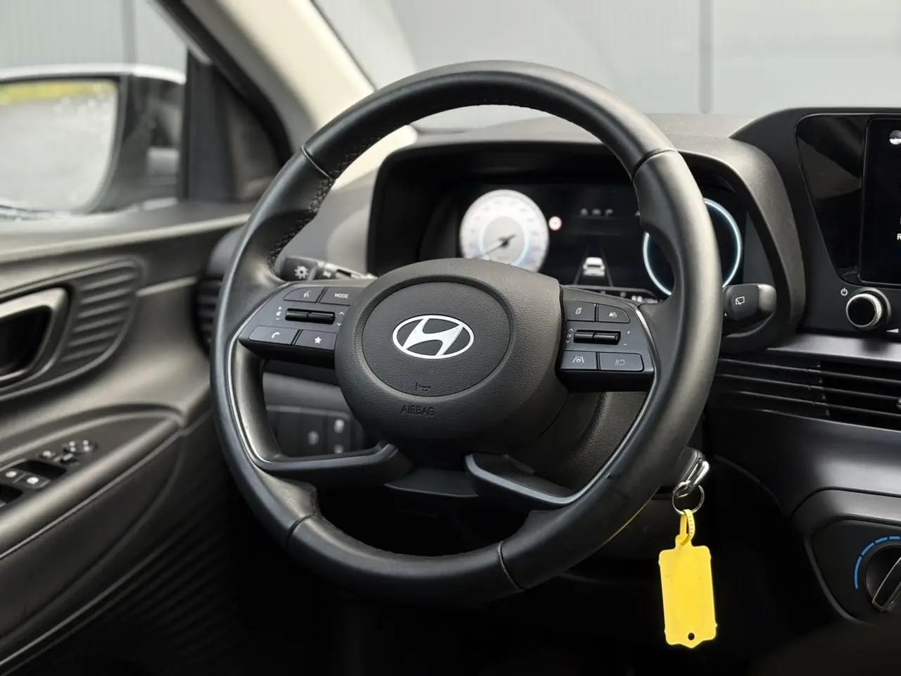 Vue intérieure centrée sur le volant cuir noir de la Hyundai i20 2025 avec tableau de bord numérique et commandes intégrées.