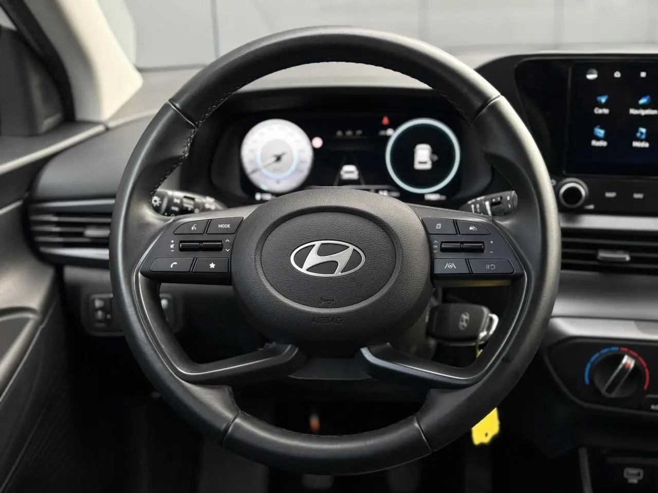 Vue rapprochée du volant cuir noir de la Hyundai i20 2025 avec commandes intégrées et tableau de bord numérique.