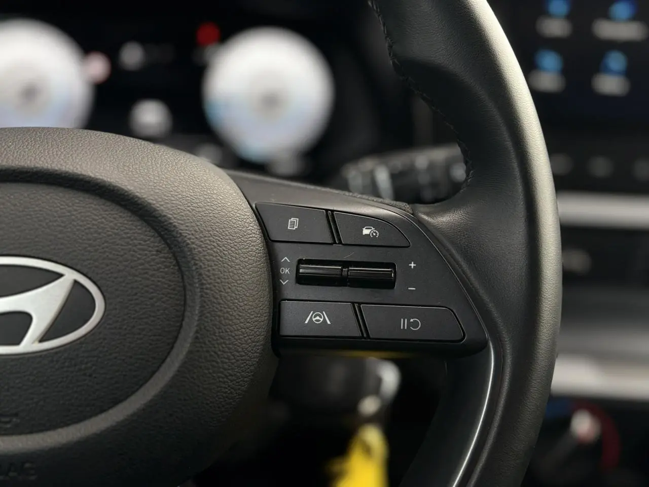 Gros plan sur le volant cuir noir de la Hyundai i20 2025, avec commandes de régulateur de vitesse et assistance au maintien de voie.