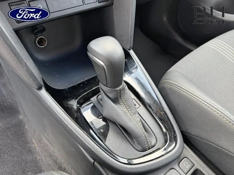 Gros plan sur la console centrale montrant le levier de vitesse automatique noir avec surpiqûres jaunes, siège tissu gris à côté.